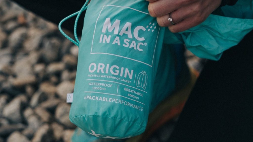 Coastal photo of a hand holding an blue origin mac in a sac for our fun in-store competition at Goulds Fashion store.